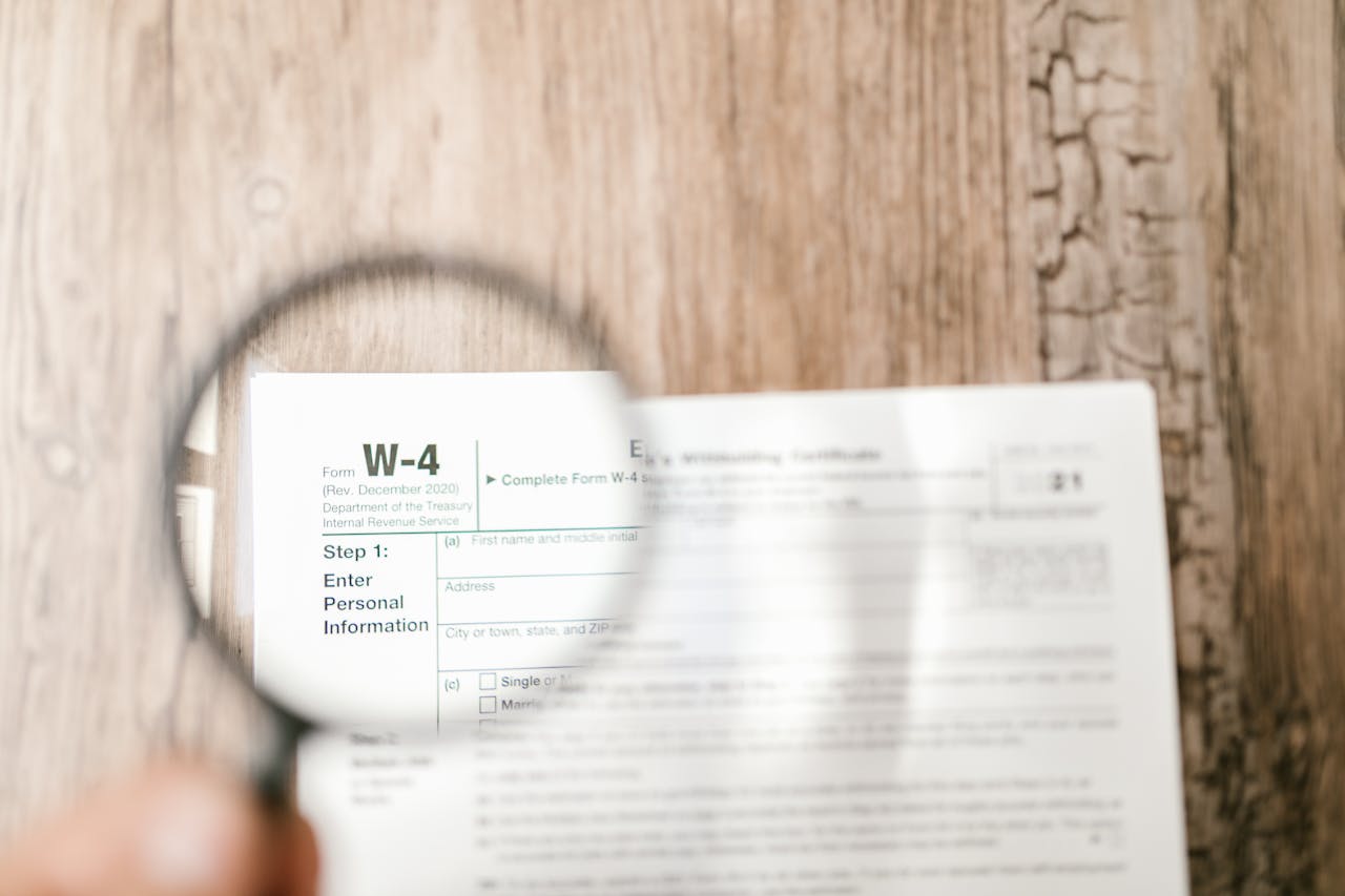 contact-hero Close-up of a W-4 tax form through a magnifying glass on a wooden table.